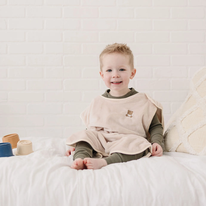 Male toddler smiling while sitting on a bed with toys.